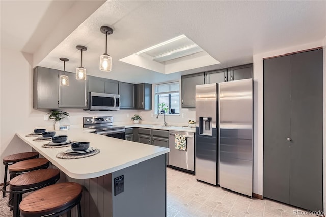 kitchen with stainless steel appliances, a peninsula, gray cabinetry, a sink, and light countertops