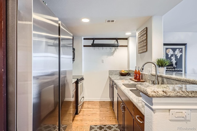 kitchen with light stone counters, a sink, light wood finished floors, stainless steel appliances, and visible vents