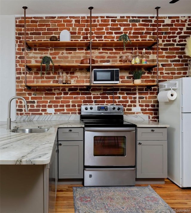 kitchen featuring stainless steel electric stove, a sink, freestanding refrigerator, gray cabinets, and light wood finished floors