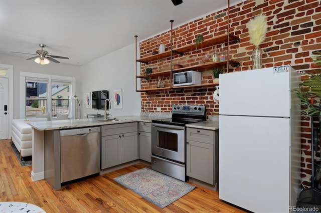 kitchen featuring stainless steel appliances, gray cabinetry, a sink, ceiling fan, and a peninsula