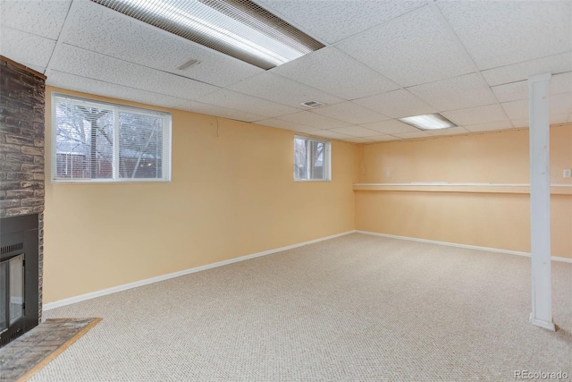 basement with a drop ceiling, a brick fireplace, and carpet flooring