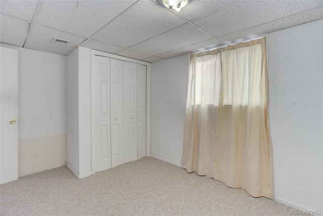 unfurnished bedroom with a paneled ceiling, carpet flooring, and a closet