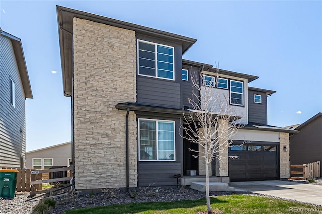 contemporary home with fence, driveway, stone siding, and a garage