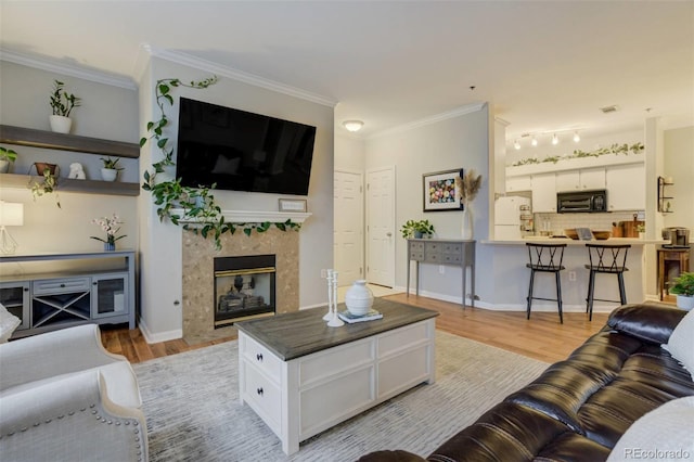 living area with ornamental molding, light wood-type flooring, a high end fireplace, and baseboards