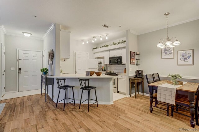 kitchen featuring stainless steel stove, visible vents, freestanding refrigerator, black microwave, and a peninsula