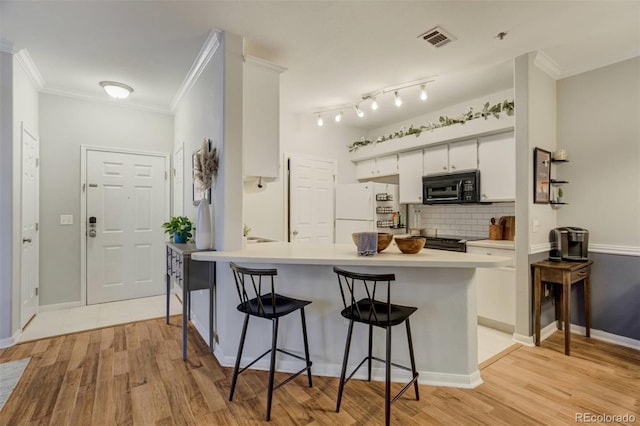 kitchen with ornamental molding, a breakfast bar area, freestanding refrigerator, a peninsula, and black microwave