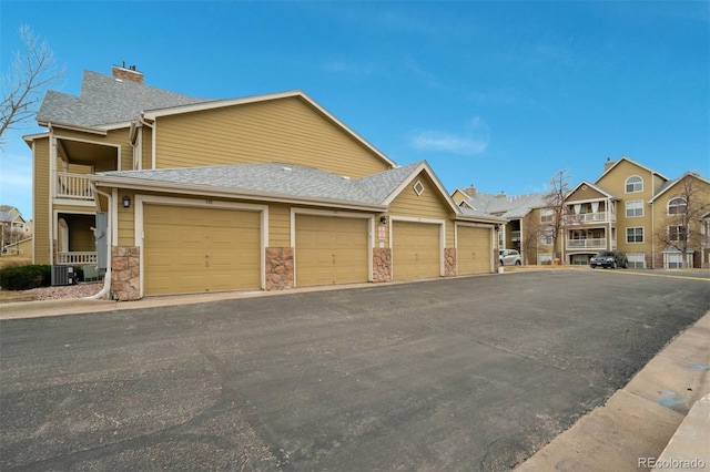 view of front of home with a balcony, community garages, stone siding, roof with shingles, and a chimney