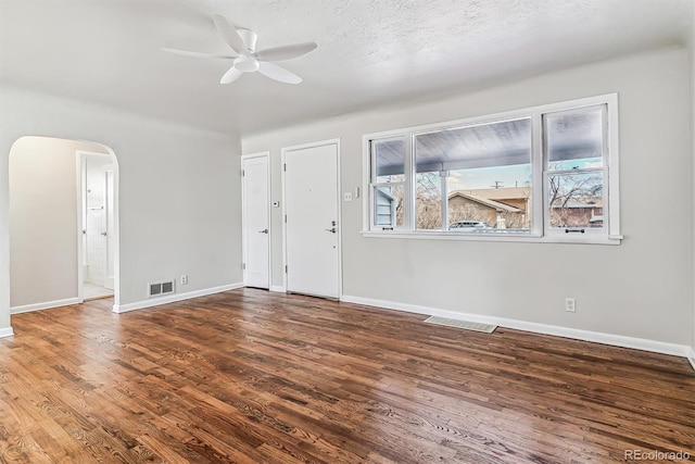 empty room featuring baseboards, visible vents, arched walkways, and wood finished floors