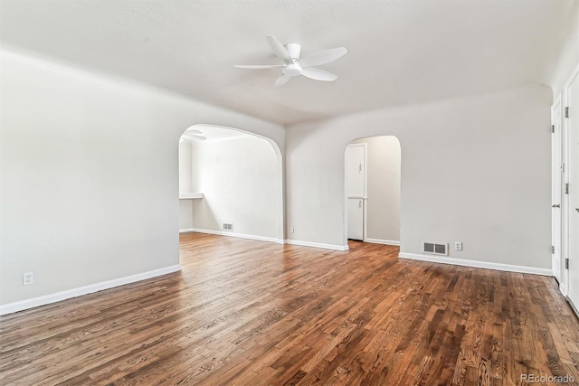 empty room featuring arched walkways, wood finished floors, visible vents, baseboards, and a ceiling fan