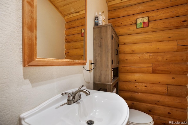 bathroom with rustic walls, sink, wooden ceiling, and toilet