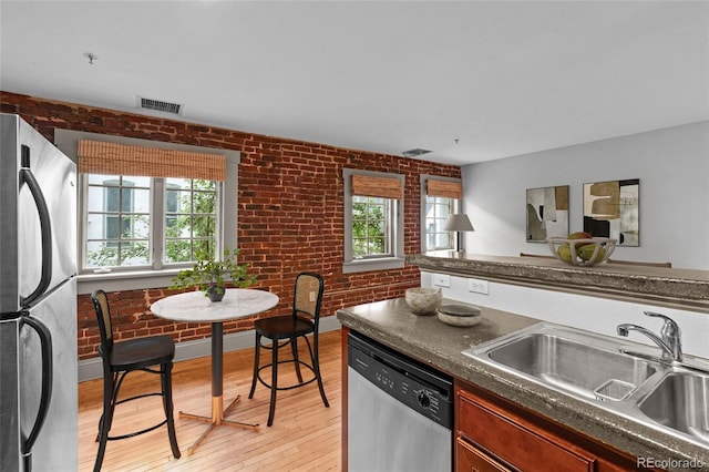 3211 Zuni St Unit 14, Denver, CO 80211 - kitchen featuring stainless steel appliances, a sink, dark countertops, brick wall, and light wood-style flooring