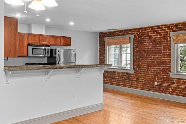 3211 Zuni St Unit 14, Denver, CO 80211 - kitchen with appliances with stainless steel finishes, a breakfast bar area, light wood-type flooring, brown cabinetry, and brick wall