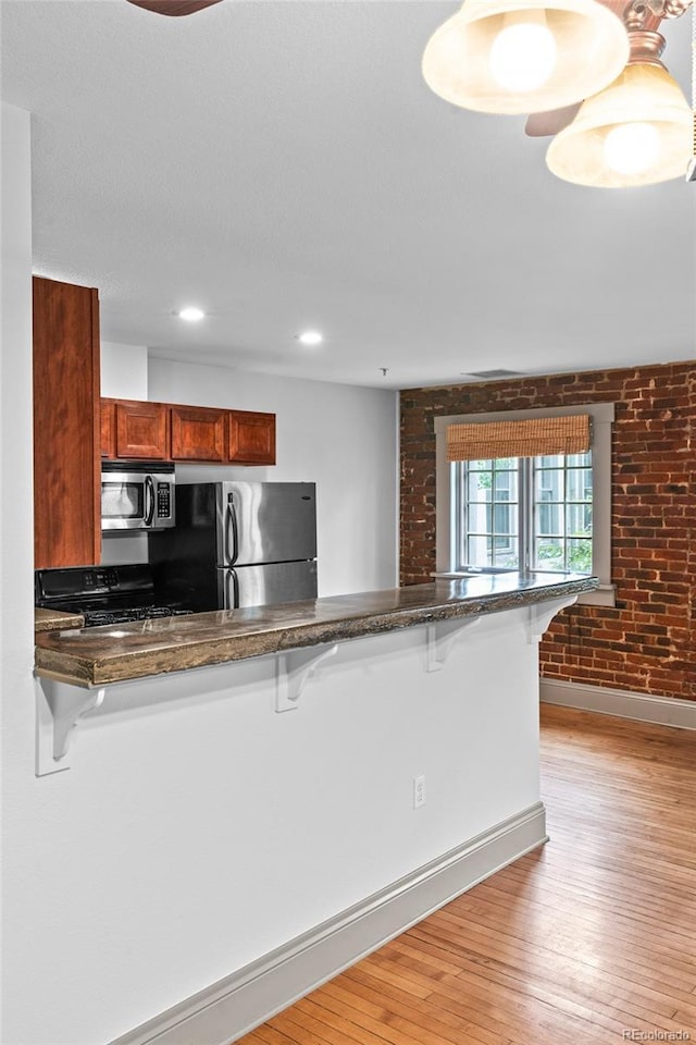 3211 Zuni St Unit 14, Denver, CO 80211 - kitchen with appliances with stainless steel finishes, a breakfast bar area, brick wall, baseboards, and light wood finished floors