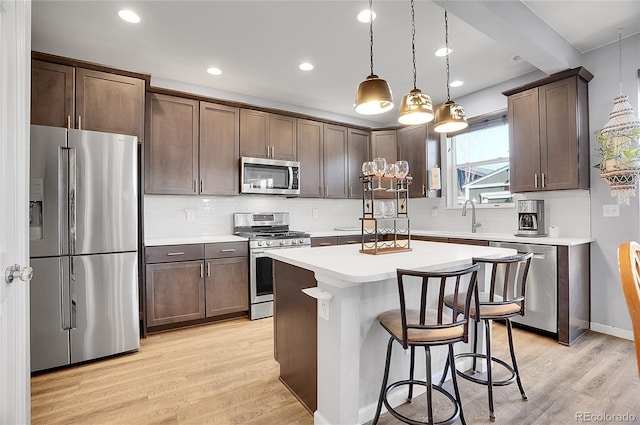 kitchen featuring appliances with stainless steel finishes, a breakfast bar, hanging light fixtures, a center island, and light hardwood / wood-style floors