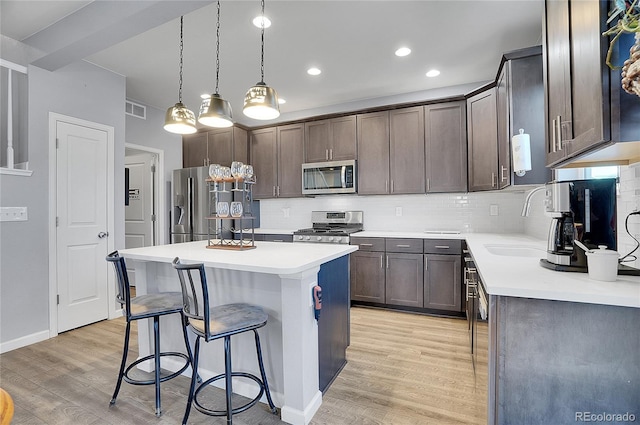 kitchen with appliances with stainless steel finishes, a kitchen island, decorative backsplash, decorative light fixtures, and light wood-type flooring