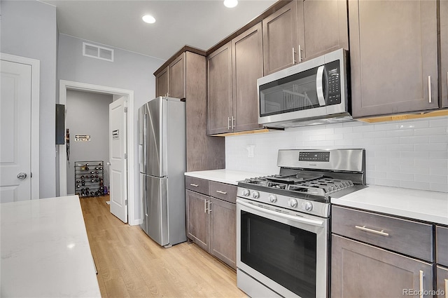 kitchen with tasteful backsplash, light wood-type flooring, dark brown cabinetry, and appliances with stainless steel finishes