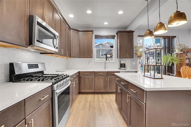 kitchen featuring tasteful backsplash, light wood-type flooring, light countertops, a center island, and appliances with stainless steel finishes