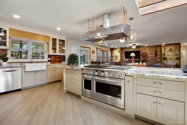 kitchen with island exhaust hood, appliances with stainless steel finishes, light stone countertops, sink, and cream cabinetry