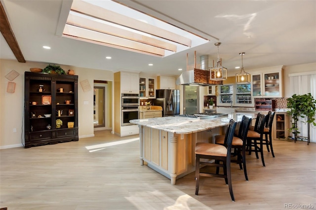 kitchen featuring pendant lighting, a skylight, light stone countertops, appliances with stainless steel finishes, and a large island