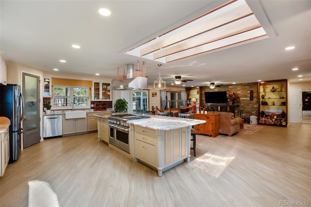 kitchen with sink, appliances with stainless steel finishes, a kitchen island, light stone counters, and island exhaust hood