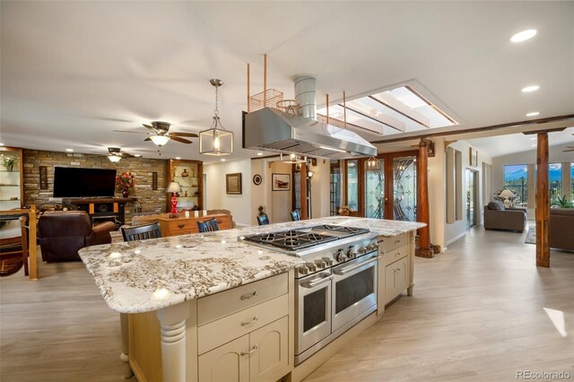 kitchen with double oven range, cream cabinets, island range hood, light stone countertops, and a kitchen island