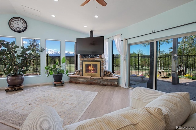 living room with hardwood / wood-style flooring, a stone fireplace, ceiling fan, and lofted ceiling