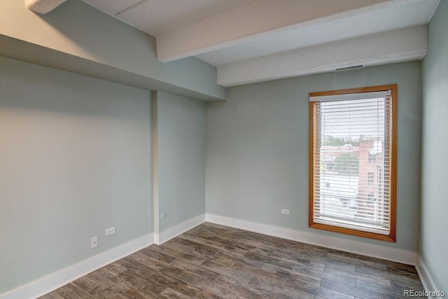 spare room featuring beam ceiling and dark hardwood / wood-style floors