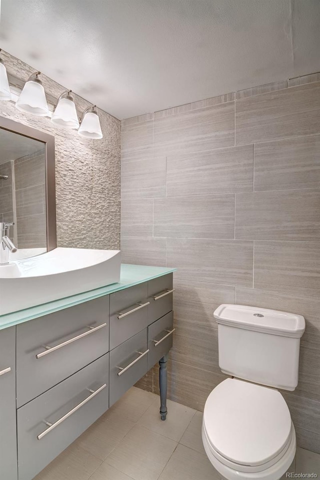 bathroom with tile patterned floors, vanity, tile walls, and toilet