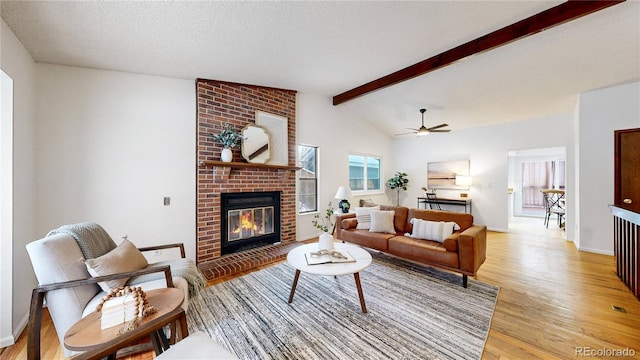 living room featuring lofted ceiling with beams, a textured ceiling, light wood-type flooring, ceiling fan, and a fireplace