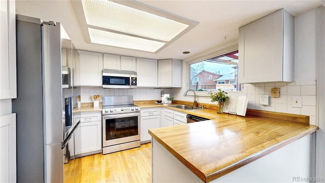 kitchen with appliances with stainless steel finishes, white cabinetry, sink, kitchen peninsula, and light wood-type flooring