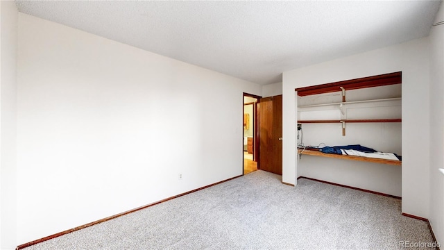 unfurnished bedroom with a closet, built in desk, light carpet, and a textured ceiling