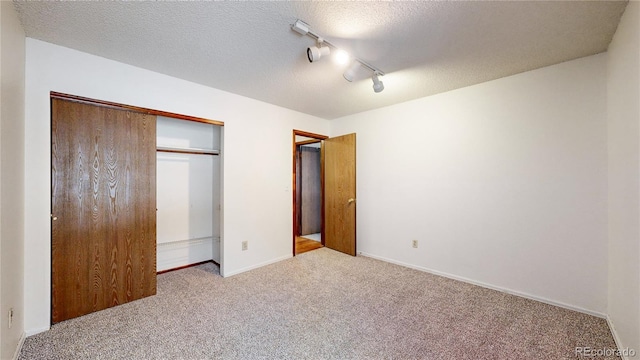 unfurnished bedroom with light colored carpet, rail lighting, a closet, and a textured ceiling