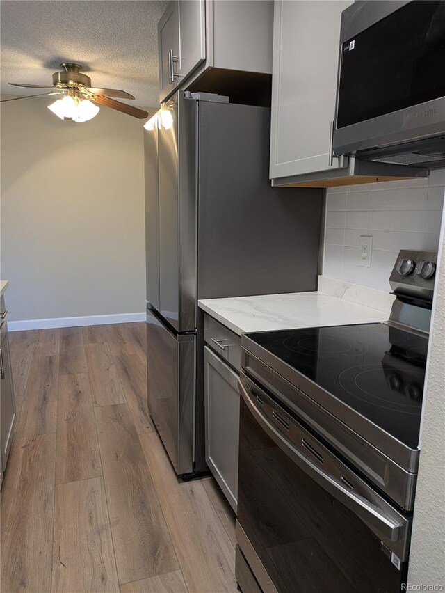 kitchen with gray cabinetry, light hardwood / wood-style floors, stainless steel appliances, and decorative backsplash