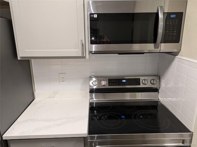 kitchen featuring white cabinetry, light stone countertops, tasteful backsplash, and appliances with stainless steel finishes