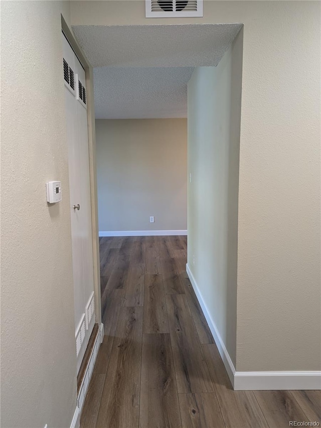 hallway with a textured ceiling and dark hardwood / wood-style flooring