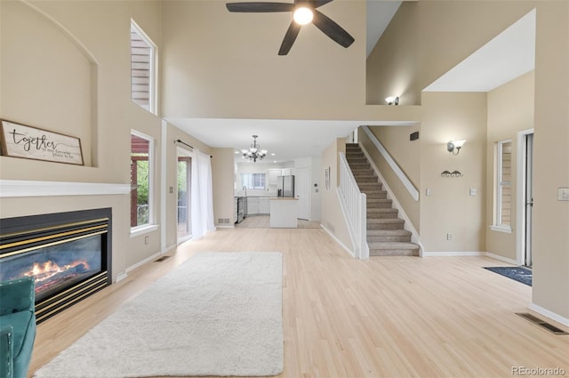 3565 W 112th Cir, Westminster, CO 80031 - unfurnished living room featuring a chandelier, stairs, a high ceiling, a glass covered fireplace, and light wood-type flooring