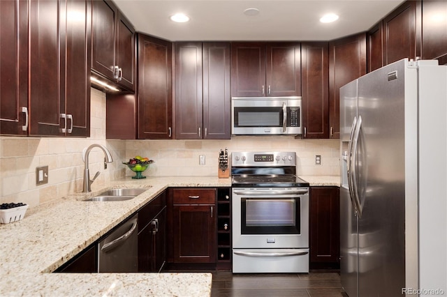 kitchen featuring light stone countertops, dark wood-style flooring, a sink, decorative backsplash, and stainless steel appliances