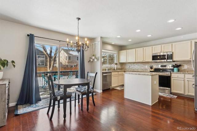 kitchen with a kitchen island, backsplash, hanging light fixtures, stainless steel appliances, and light stone countertops