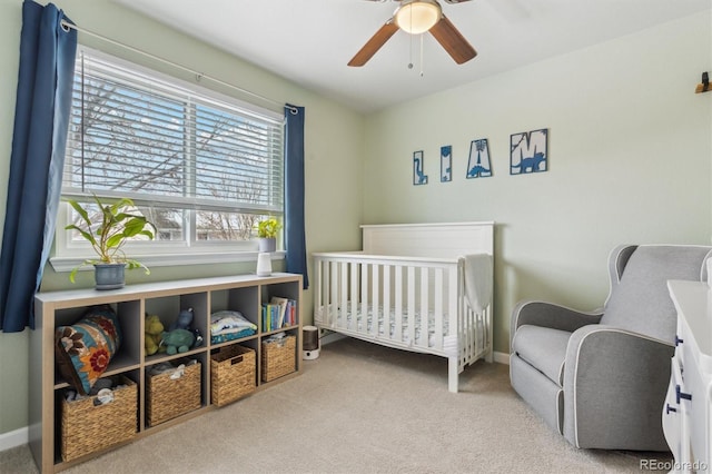 carpeted bedroom featuring a nursery area and ceiling fan