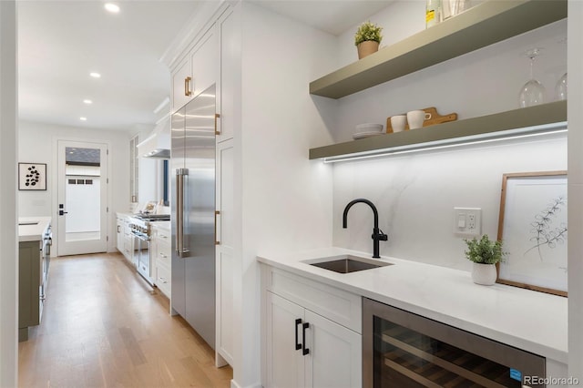 kitchen with white cabinetry, sink, beverage cooler, premium appliances, and light wood-type flooring