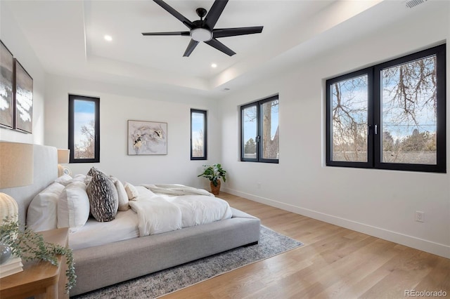 bedroom with a tray ceiling, light hardwood / wood-style flooring, and ceiling fan