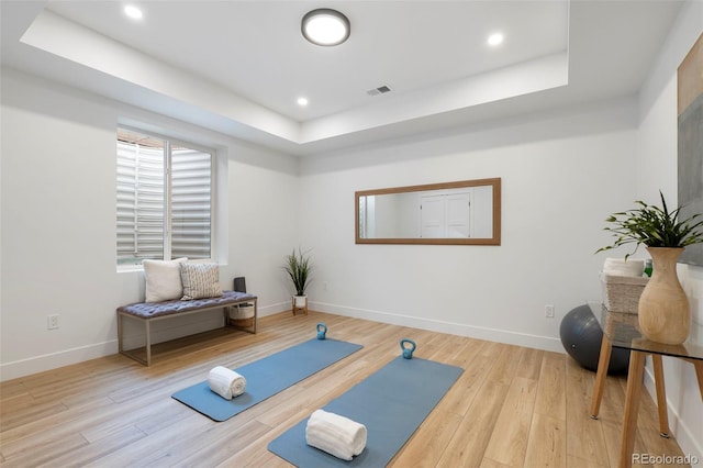 exercise area featuring a raised ceiling and light hardwood / wood-style flooring