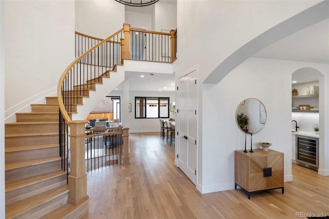 entrance foyer with wine cooler, a towering ceiling, light hardwood / wood-style flooring, and indoor wet bar