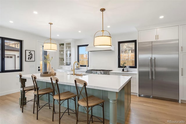 kitchen featuring a breakfast bar area, white cabinetry, decorative light fixtures, appliances with stainless steel finishes, and a kitchen island with sink