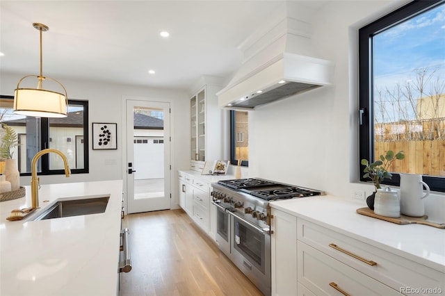 kitchen featuring sink, white cabinetry, hanging light fixtures, custom range hood, and range with two ovens