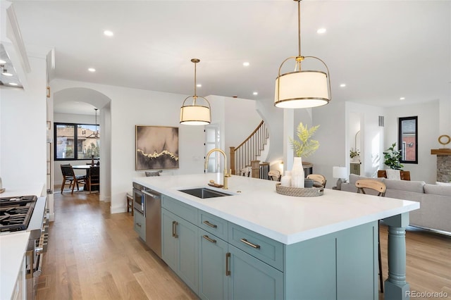 kitchen featuring decorative light fixtures, a kitchen island with sink, sink, and light wood-type flooring