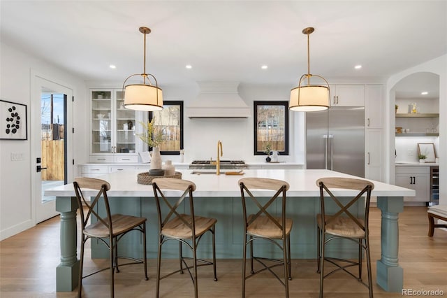 kitchen with pendant lighting, a breakfast bar area, built in refrigerator, custom range hood, and a spacious island