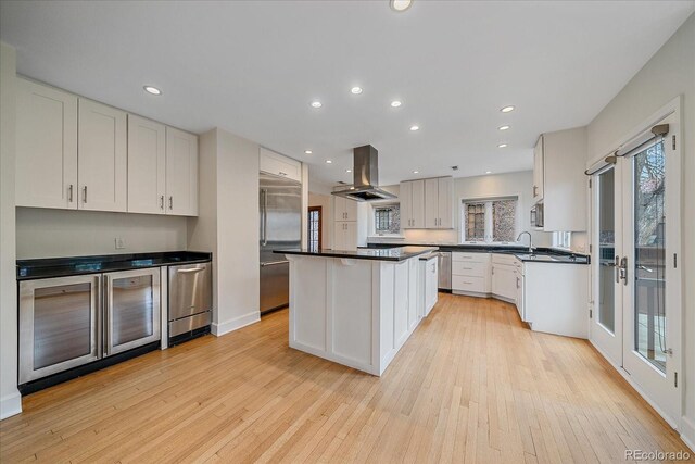 371 Birch St, Denver, CO 80220 - kitchen with dark countertops, island exhaust hood, white cabinetry, light wood finished floors, and appliances with stainless steel finishes