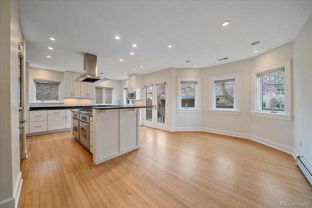 371 Birch St, Denver, CO 80220 - kitchen featuring light wood-type flooring, dark countertops, baseboards, white cabinetry, and island range hood