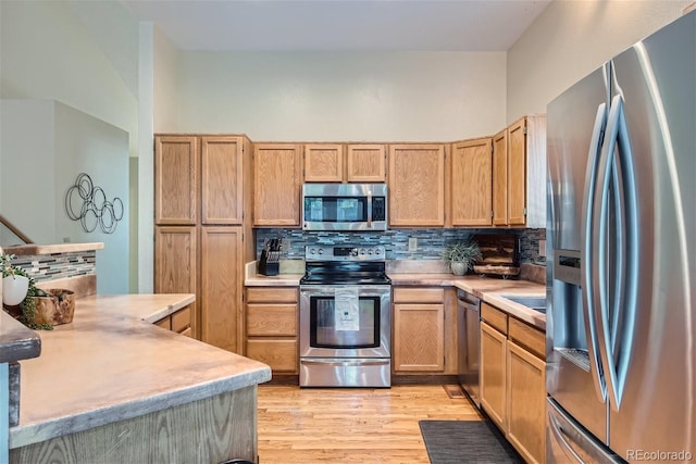 kitchen with decorative backsplash, appliances with stainless steel finishes, a high ceiling, and light hardwood / wood-style floors